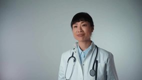 Attractive Asian female doctor with a white coat smiling and holding an apple and orange. Cheerful medical nutritionist recommending a healthy diet to a patient, 4k video footage.