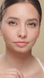 Beauty brunette woman applying lip gloss isolated on beige background. Vertical video. Makeup cosmetics