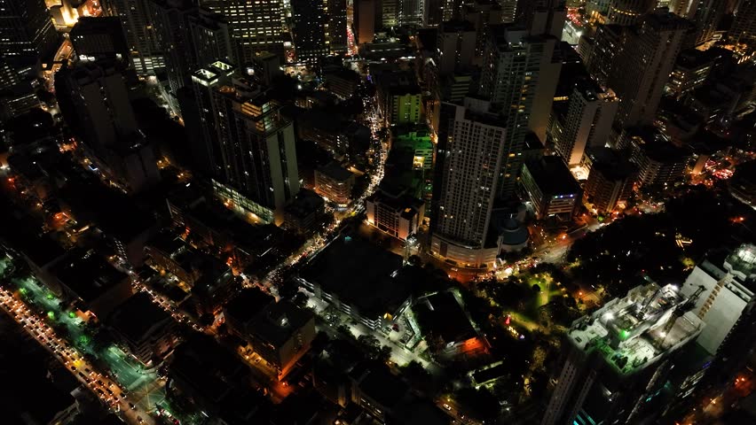 Flying over the modern buildings and colorful streets. Makati City at Night. Metro Manila. Philippines.
