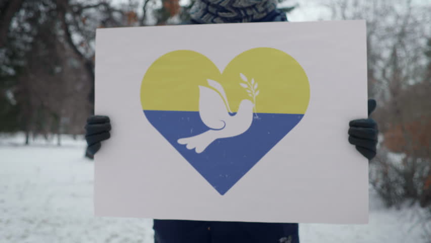 Holding a banner in support of peace on the Ukraine territory. Demonstrator supporting the Ukrainian people by carrying a peace placard. Supporter asking for peace in the Ukraine. No To War. Royalty-Free Stock Footage #3445374035