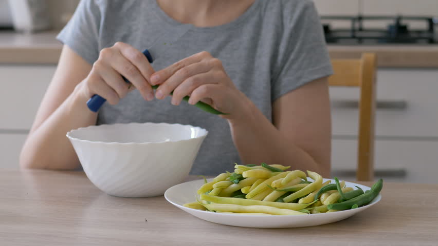Woman cuts the tips of green and yellow beans and prepares vegetable meal