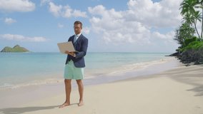 Confident caucasian man in suit and beach shorts holding open laptop in hands, standing barefoot on warm sand of the Hawaiian island over azure ocean. High quality 4k footage
