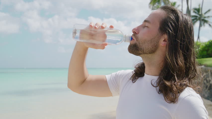 Handsome male tourist with light unshaveness enjoying vacation on the beach of Hawaii gazing at aquamarine waters of the Pacific ocean and vast horizon. High quality 4k footage Royalty-Free Stock Footage #3445406595