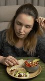 Woman sitting on a chair and enjoying eating homemade vegan tacos with jackfruit, avocado, and pico de gallo salsa. Vertical video.