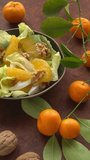 Orange salad with orange fruit, romaine lettuce and walnut nuts. Small tangerines on the green branches with leaves on the side. Fresh, homemade salad, table spin. Vertical video.