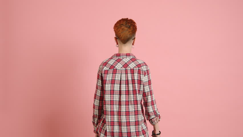 An LGBTQ advocate stands with their back turned, swiftly swinging a vibrant rainbow flag before turning with a broad, exultant smile towards the camera against a pink backdrop. Camera 8K RAW. 