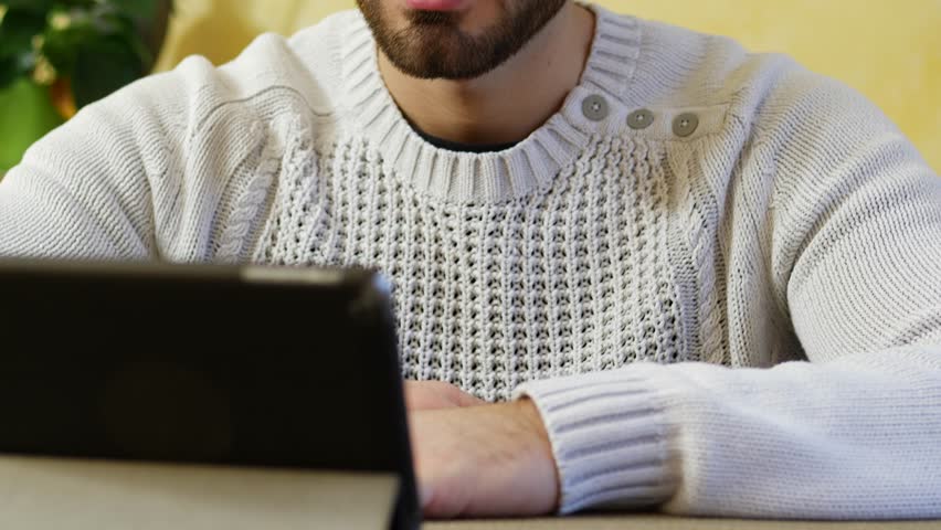 Attractive young man using tablet PC to watch video or movie, while sitting at table at home