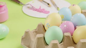A female hand is putting an Easter egg painted in pink color and flower pattern in an egg container. Many colorful Easter eggs with different patterns featured with a palette knife. Easter Day content