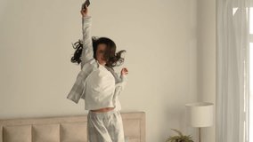 Happy young Caucasian woman jumping bed holding smartphone mobile phone joyful carefree cheerful girl weekend leisure home morning music bedroom excited mattress enjoy holiday energetic fun domestic - Powered by Shutterstock - Get 15% off with code: PIKWIZARD15