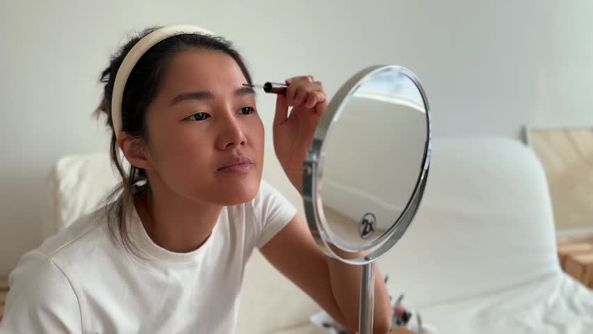 Asian woman in white t-shirt wearing make up in the living room.