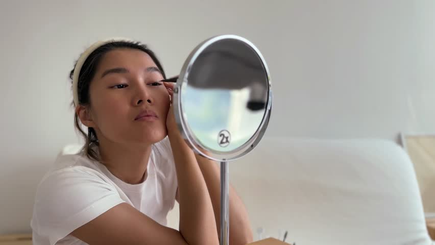 Asian woman in white t-shirt wearing make up in the living room.