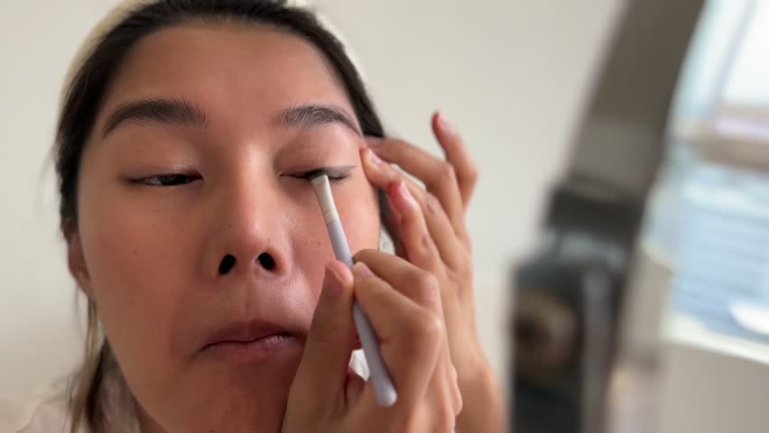Asian woman in white t-shirt wearing make up in the living room.