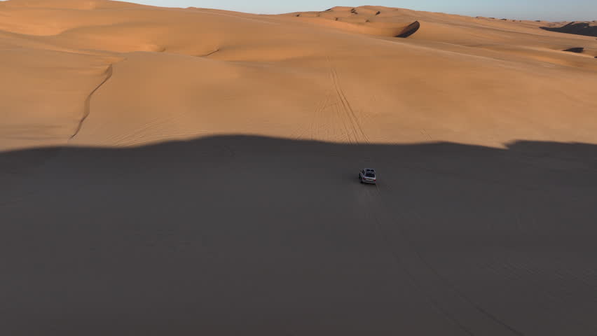 Aerial drone view of a 4x4 car driving fast through the high dunes on a beautiful sunset in Sandwich Harbour, Namibia, Africa Royalty-Free Stock Footage #3445618595