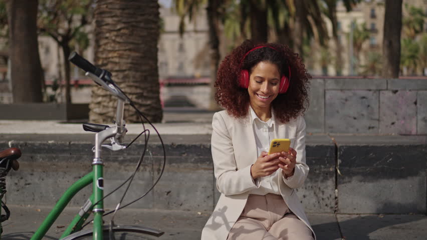 businesswoman listening music oudoors in a park with headphones and smartphone, close to her bike
