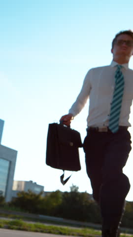 SLOW MOTION, LENS FLARE, BOTTOM UP: Young businessman in a hurry jumps over the camera as he runs to his office building. Excited Caucasian man rushing to get to an important business meeting on time. Royalty-Free Stock Footage #3445671577