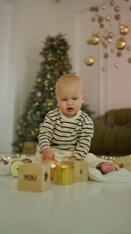 Toddler Enjoing Christmas Festivities. Young child in festive attire plas vith Christmas ornaments and gifts by tree.
