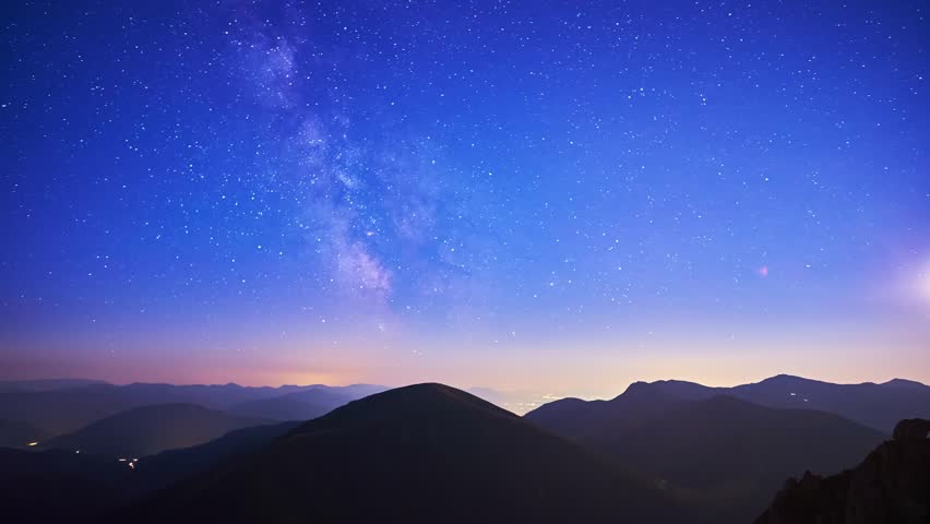 Time lapse of the Milky Way, the silhouette of the mountain landscape, the night city shining in the valley Royalty-Free Stock Footage #3445722583