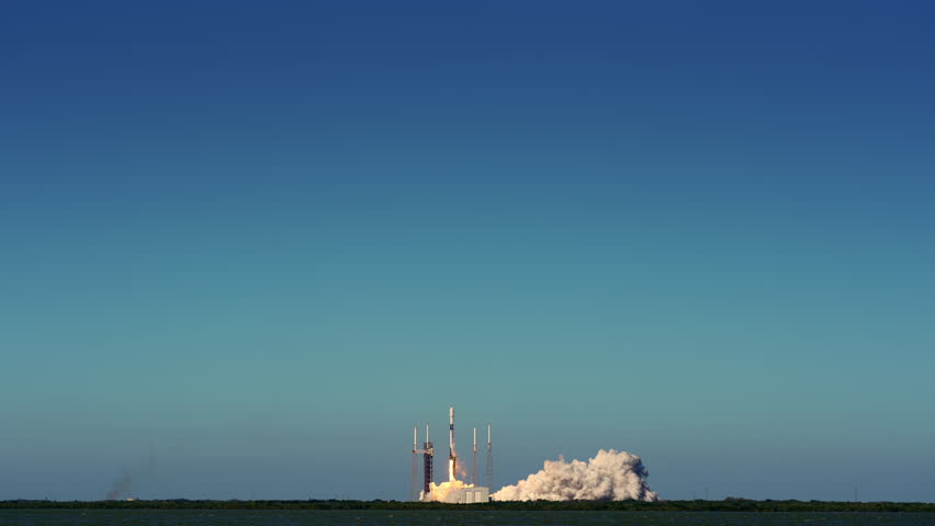 Rocket lifts off from launch pad and rises into a clear blue sky. Wide shot. Slow-motion with sound.