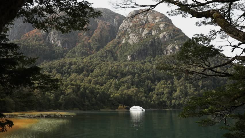 Patagonia tourism. View of a yacht in the turquoise color glacier lake surrounded by the forest and mountains in Puerto Blest, Nahuel Huapi national park, Bariloche, Argentina.
