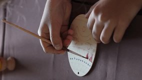 Vertical video. Close-up of little girl painting wooden Easter egg in the kitchen