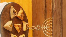 Gomentashi cookies for Purim rotate in a circle on a wooden board next to the treshoti and menorah.Vertical video