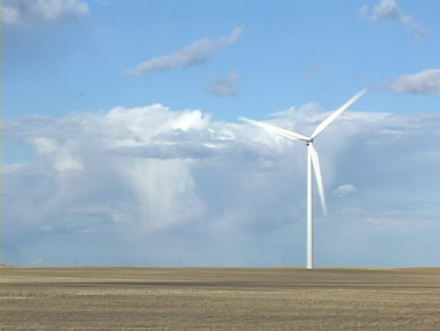 Wind turbine in open field with blue sky and clouds