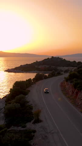 DRONE: Tourists on sightseeing road trip exploring the Mediterranean island at picturesque sunset. Flying along the scenic rocky shoreline of Lefkada at sunset and car driving down the coastal road.