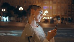 Cheerful lady scrolling cellphone at night city closeup. Happy short hair woman texting cellphone waiting meeting on evening street. Trendy informal girl watching social media standing dark urban area - Powered by Shutterstock - Get 15% off with code: PIKWIZARD15