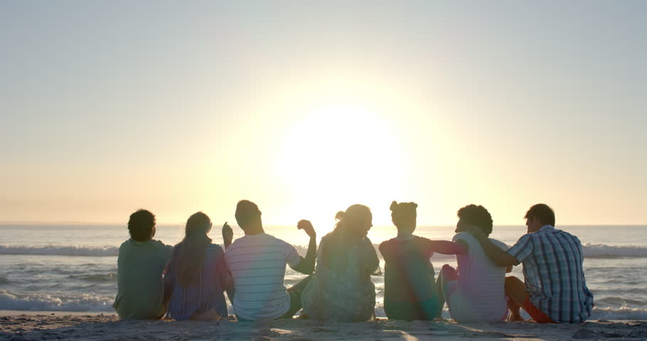 Diverse group of friends enjoy a serene beach sunset, with copy space. They sit close together, embracing the peaceful outdoor moment, slow motion. Royalty-Free Stock Footage #3446102287