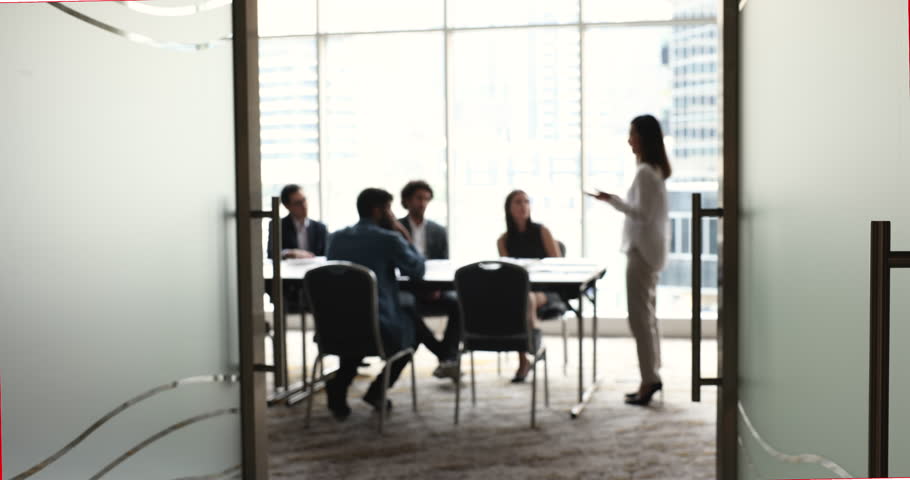 Defocused view team of businesspeople talking during briefing in board room led by female boss share ideas, strategy, planning cooperation with clients, engaged in formal meeting workflow in office