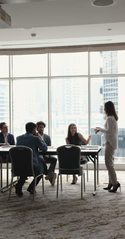 Multinational team take part in group briefing met in modern skyscraper office board room, vertical view. Diverse businesspeople talk about collaborative project sit at desk listen to business trainer Royalty-Free Stock Footage #3446189591