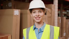 A girl in a warehouse in a hard hat is smiling