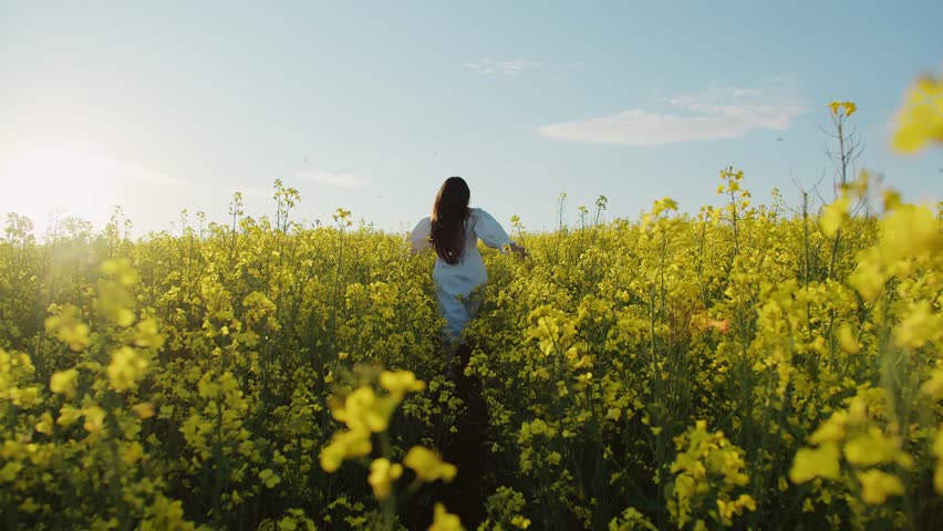 A girl in a dress runs through a field of yellow flowers