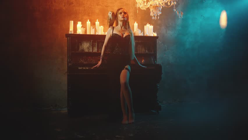 Art fantasy style gothic woman standing near piano old retro white black keys, dark classic room. Girl in luxury black dress fashion model posing looking at camera beauty lady sexy face. barn Owl bird