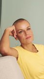 Vertical video, Beautiful bald woman dressed in yellow T-shirt and jeans sitting in living room, enjoying free time on weekend