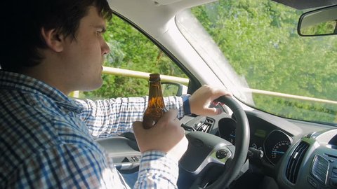 Slow motion video of irresponsible male driver drinking alcohol while driving car