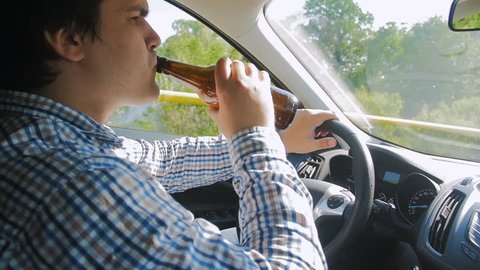 Slow motion video of man drinking beer from bottle while driving car. Irresponsible driver. Don't drink while driving