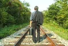 Video of a business man walking away on an empty railroad track throwing away is suitcase and jacket.
