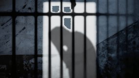 Silhouette: a desperate man, hands pressed against his face, his back bowed under the weight of troubles, confined behind shadowed prison bars, his image cast upon a weathered wall.
 - Powered by Shutterstock - Get 15% off with code: PIKWIZARD15