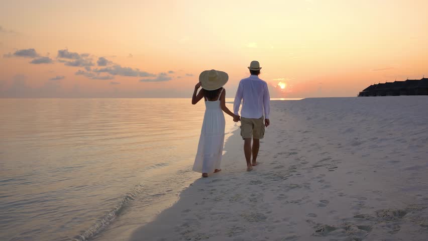 A beautiful couple walks along a tropical paradise beach and watches the sunset in the Maldives islands