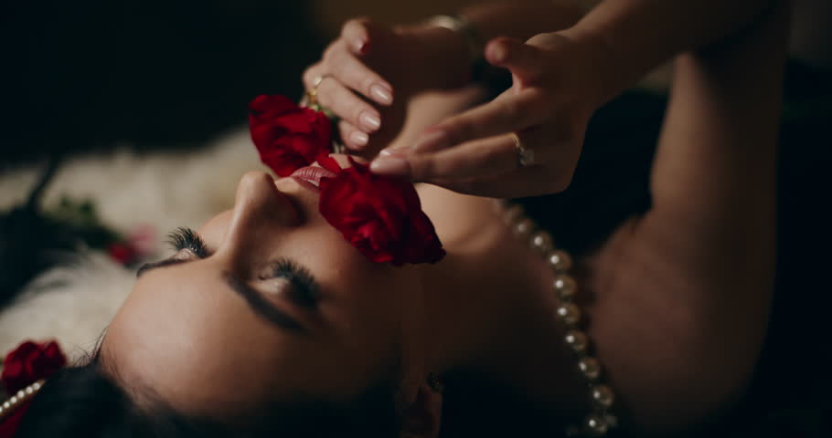 Closeup shot of seductive young woman smelling and touching face with red roses while lying on bed