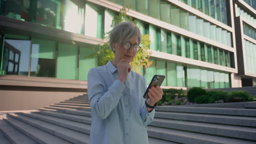 Senior happy businesswoman Caucasian female hold mobile phone gadget in city outdoors excited amazed middle-aged adult 50s old business woman win smartphone online victory dancing celebrate success Royalty-Free Stock Footage #3446532001