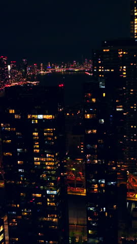 Light in the windows of the buildings in New York. Bridge over the dark river and metropolis skyline at backdrop. Vertical