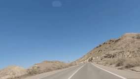 First person view, FPV, from dashcam of car driving in the Tabernas desert in Almeria, Andalusia, Spain. Arid setting of spaghetti western films. Road trip video in POV, with bright, sunny, clear sky