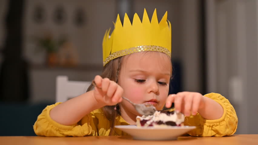 Little cute toddler girl in a yellow dress with a crown on her head eats a cake. Footage for a holiday or birthday