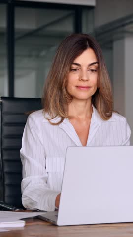 40s mid age European business woman CEO using laptop application for work at workspace in office. Smiling Latin Hispanic mature adult professional businesswoman using pc digital computer. Vertical Royalty-Free Stock Footage #3446629811