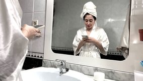 Video of portrait of a young latina woman chatting on her cell phone in front of the mirror at home before having a beauty treatment.