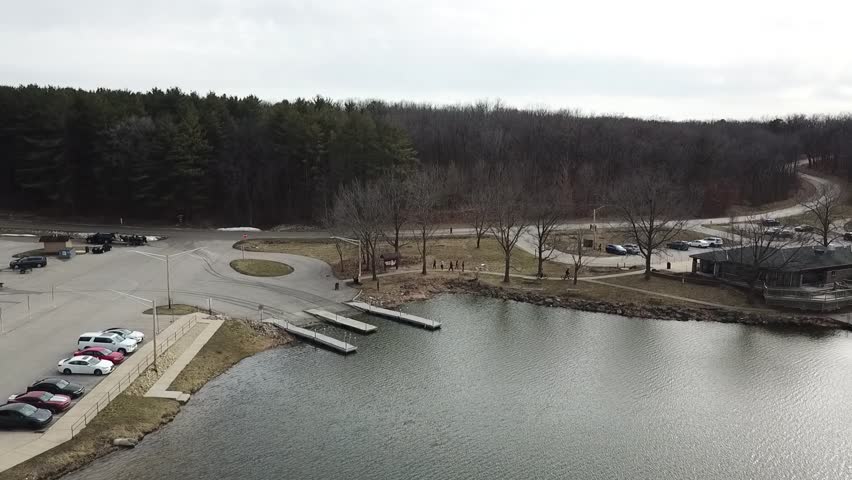 4k high resolution panning aerial drone video of water at a lake and bare trees close to the shoreline and 3 boat ramps and a building.