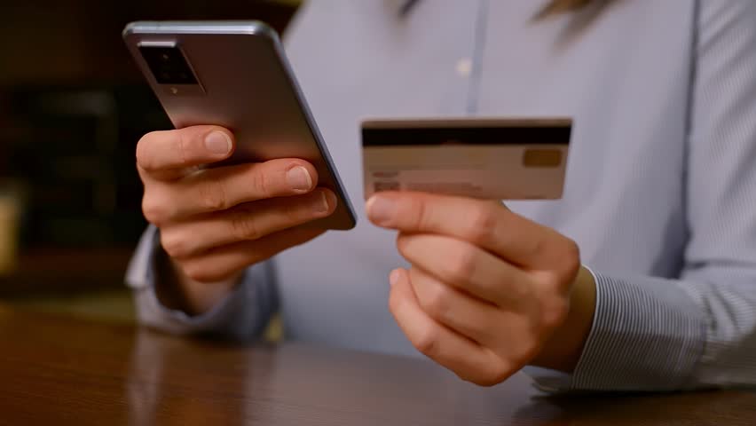 A close-up of woman uses e-bank application for banking on wireless device. Female hands navigate a smartphone, holding a credit card, performing instant remote payments, money transfers.  Royalty-Free Stock Footage #3446704709