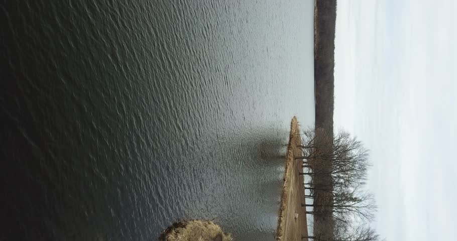 4k high resolution vertical aerial drone video of water at a lake and bare trees close to the shoreline.